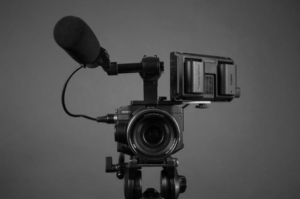 Black and white front view of a professional Sony video camera rig with a microphone and monitor mounted on a tripod